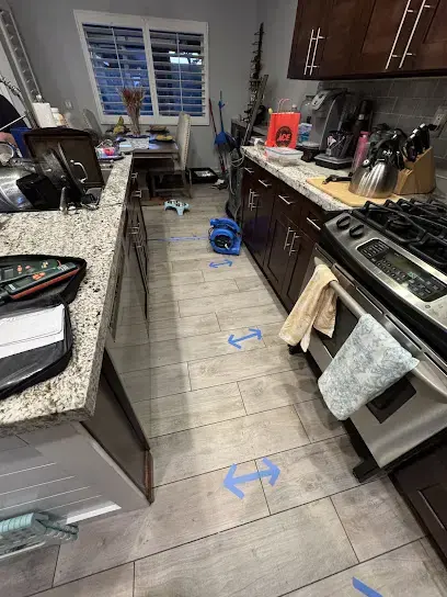 Blue tape arrows marking the wet footprint on a Lake Elsinore kitchen floor during moisture mapping